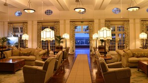 A spacious lobby with multiple seating areas, large windows, and decorative lighting fixtures. - The Victoria Falls Hotel (Victoria Falls)
