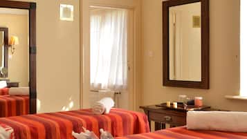 Two beds are dressed in striped bedspreads, accompanied by a large mirror and a nightstand with a lamp and decorative items.