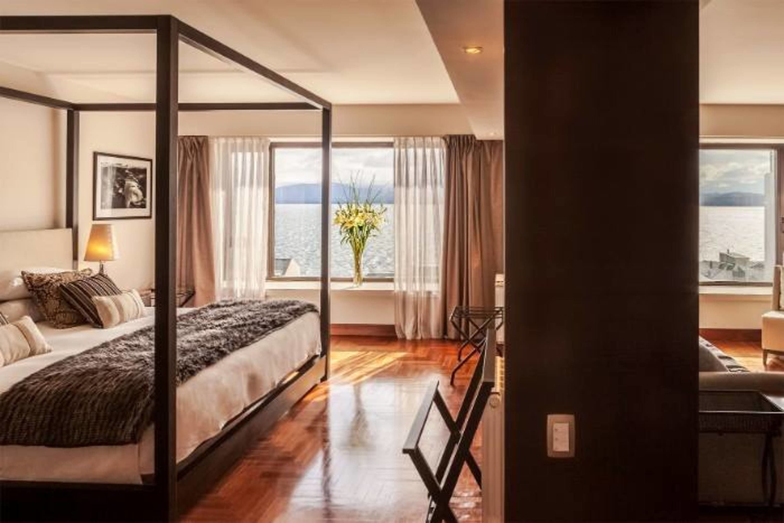 A four-poster bed with a view of the lake, a vase of flowers, and a wooden floor.