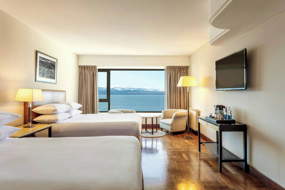 Une chambre d’hôtel avec deux lits, un bureau avec une lampe, une chaise, une petite table et un téléviseur.