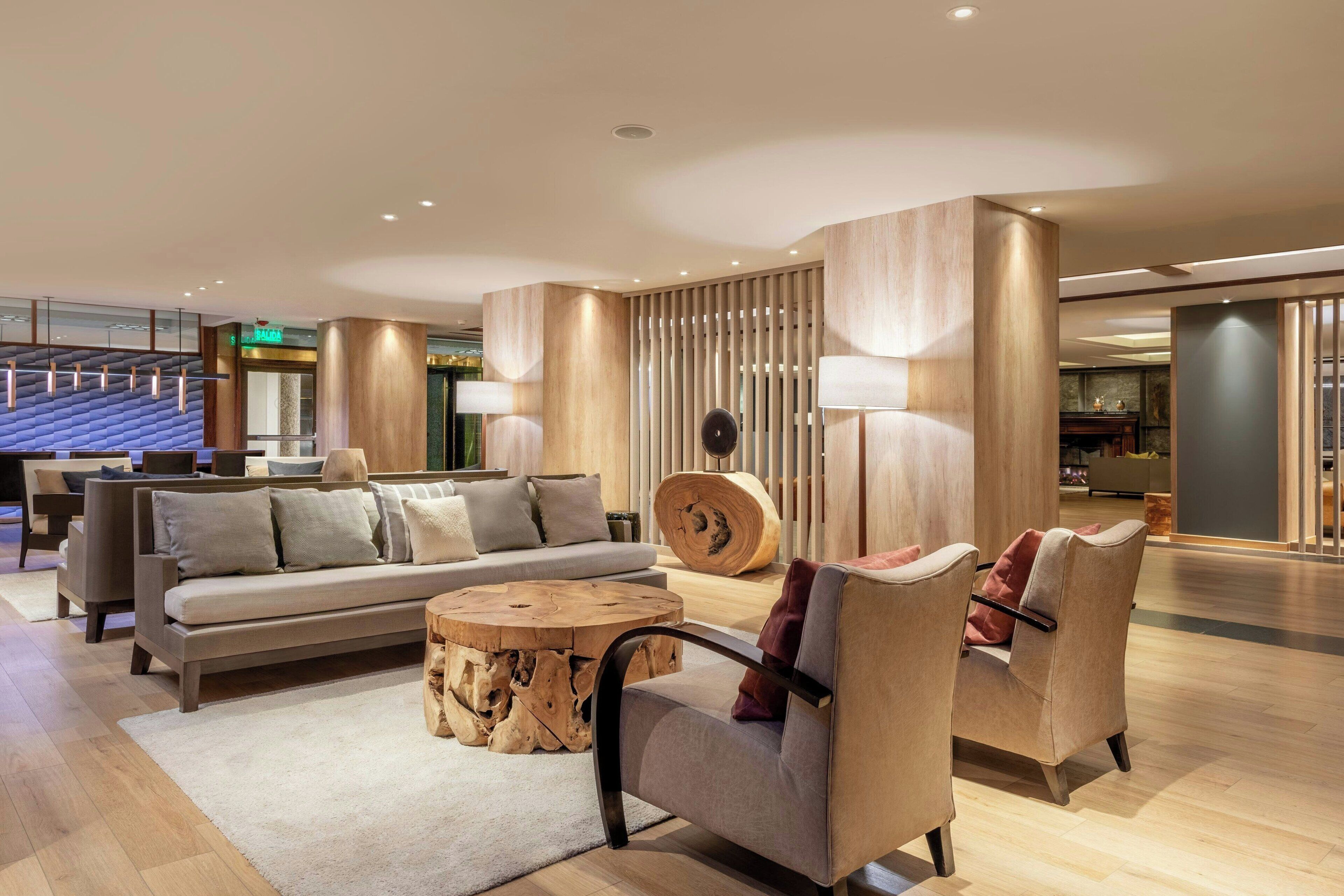 Een moderne hotellobby met een bank, stoelen, een ronde salontafel en een houten accentmuur.