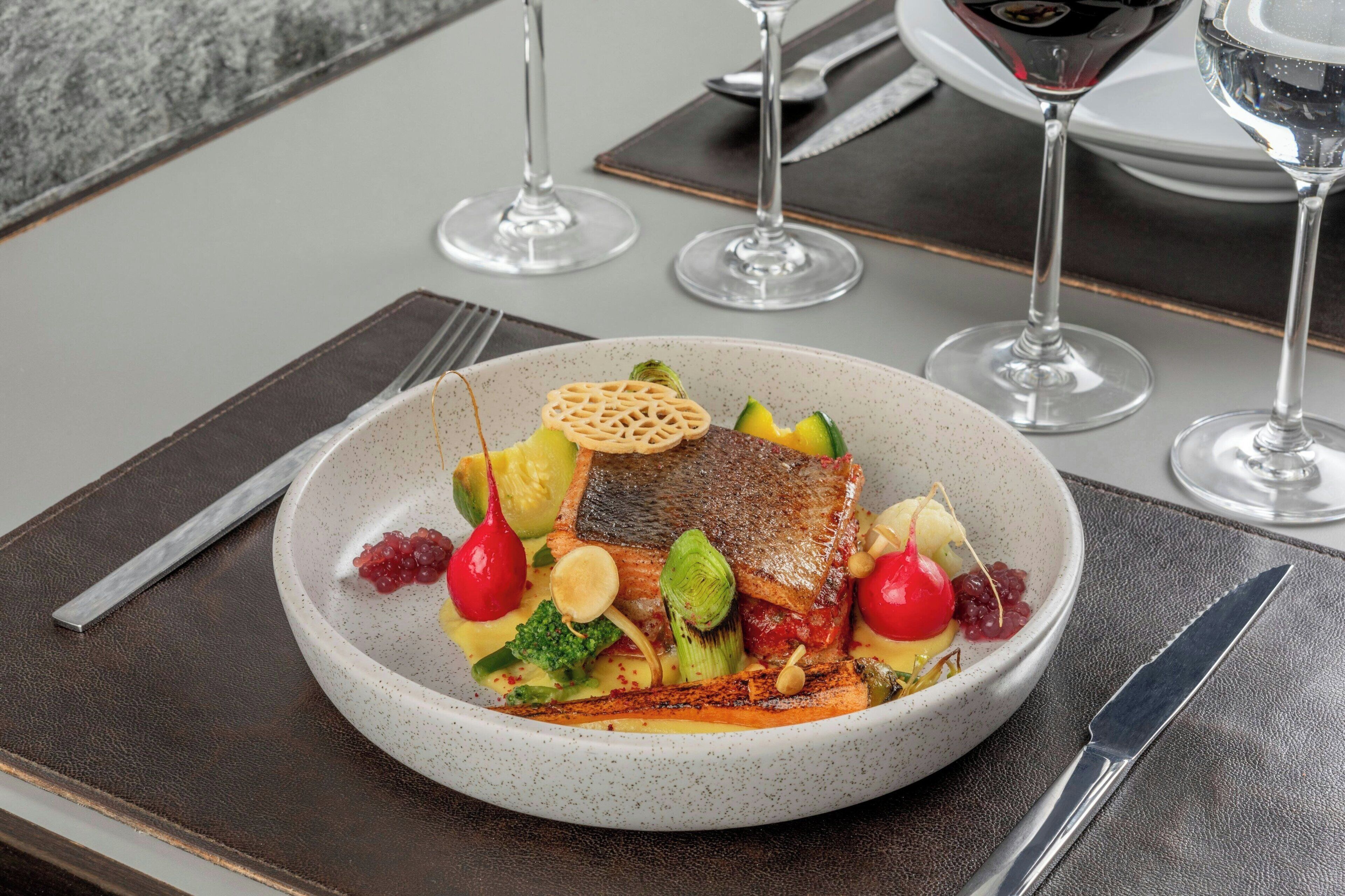 A dining table with a plate of food, a fork, a knife, and two wine glasses.
