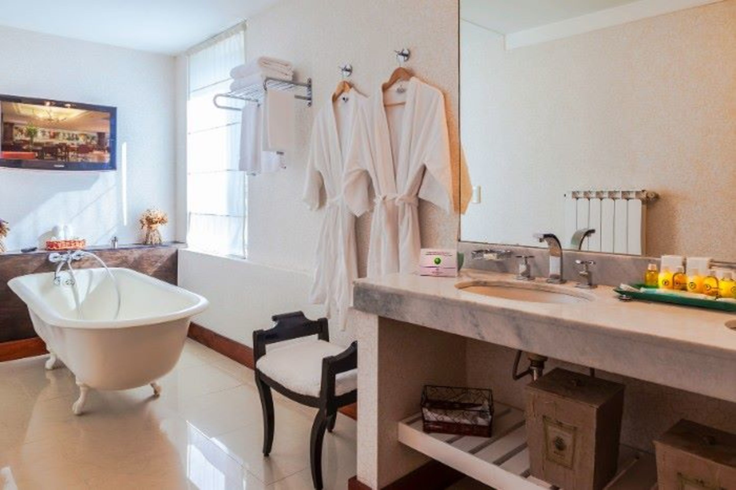 Un baño con una bañera independiente, un tocador con espejo y dos albornoces blancos colgados en ganchos.