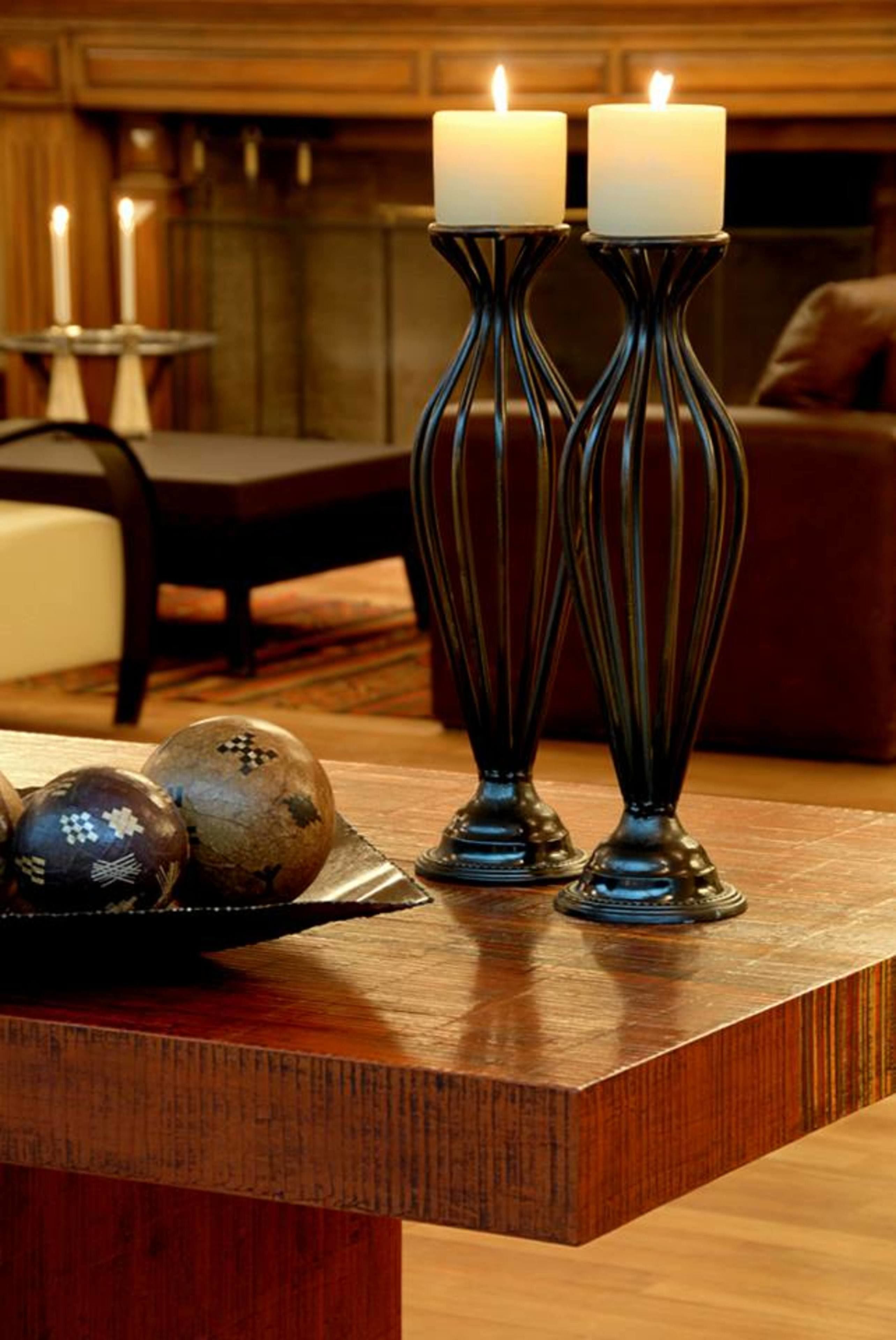 A wooden table with two candles in decorative holders, a bowl with decorative balls, and a dining area in the background.