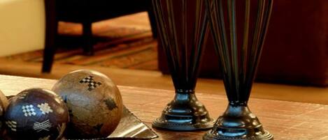 A wooden table with two candles in decorative holders, a bowl with decorative balls, and a dining area in the background.