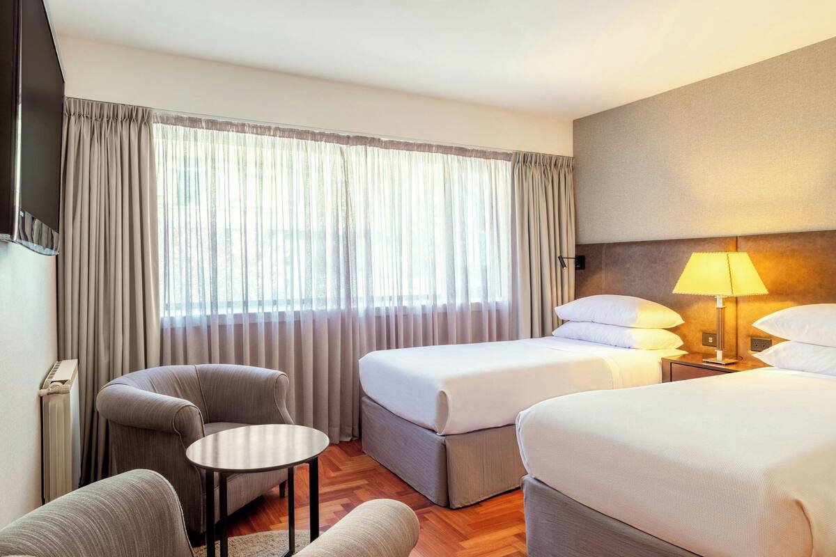 Une chambre d’hôtel avec deux lits, un canapé, une petite table et une lampe.