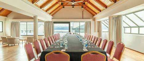A conference room with a long table, red chairs, and a wooden ceiling.