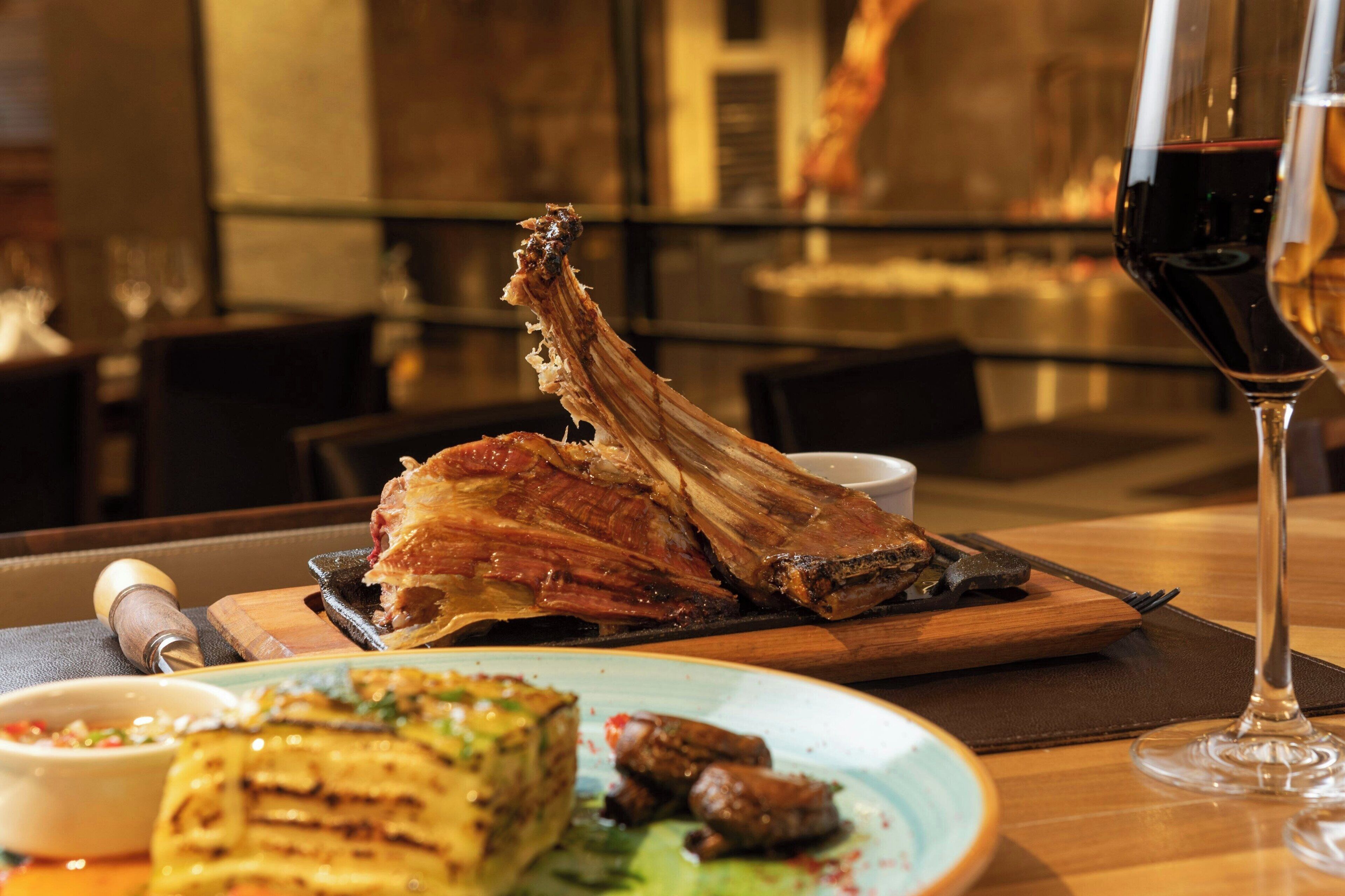 A dining table with a roasted leg of lamb, a plate of food, and a glass of red wine.