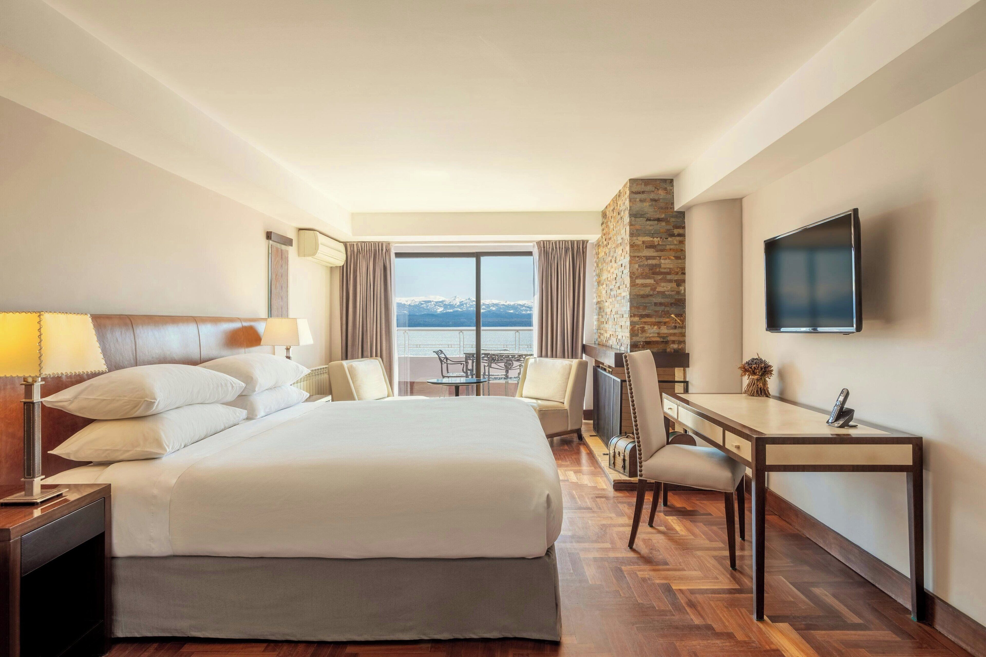 Habitación de hotel con una cama grande, un escritorio, una silla, un televisor y vistas al exterior.