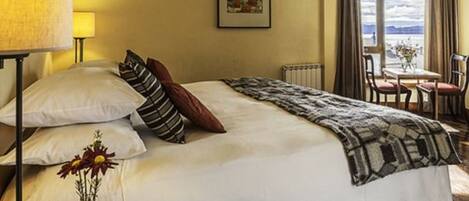 Habitación de hotel con cama, una mesa con sillas, una ventana con cortinas y un cuadro en la pared.