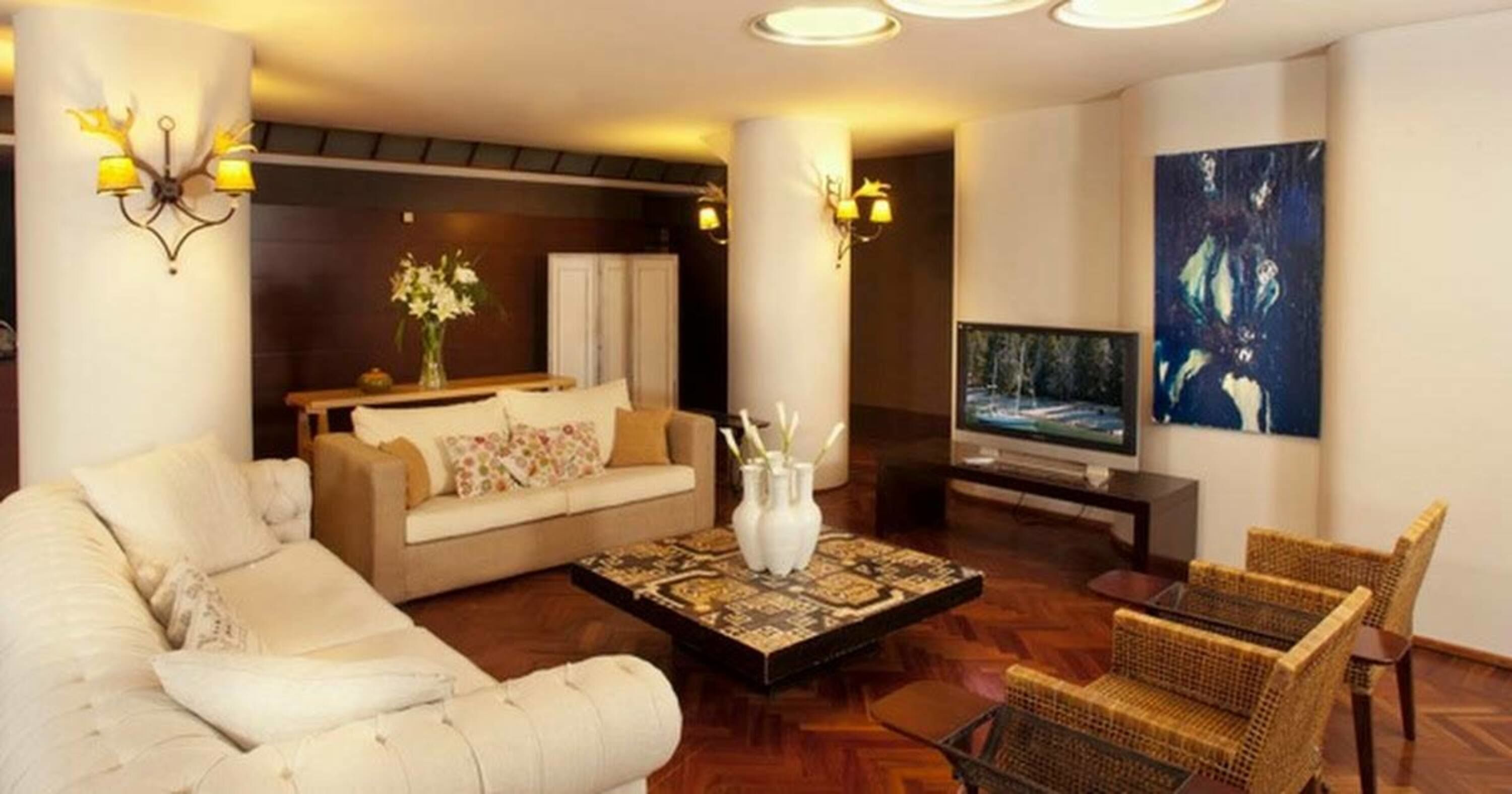 Een moderne woonkamer met een bank, een salontafel en een televisie. Op de salontafel staan decoratieve vazen en aan de muur hangt een schilderij.