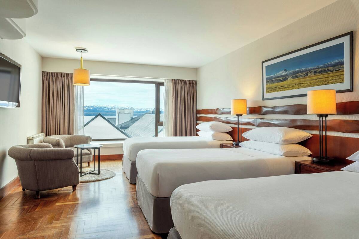 Une chambre d’hôtel avec deux lits, un canapé, une petite table et une grande fenêtre donnant sur les montagnes.