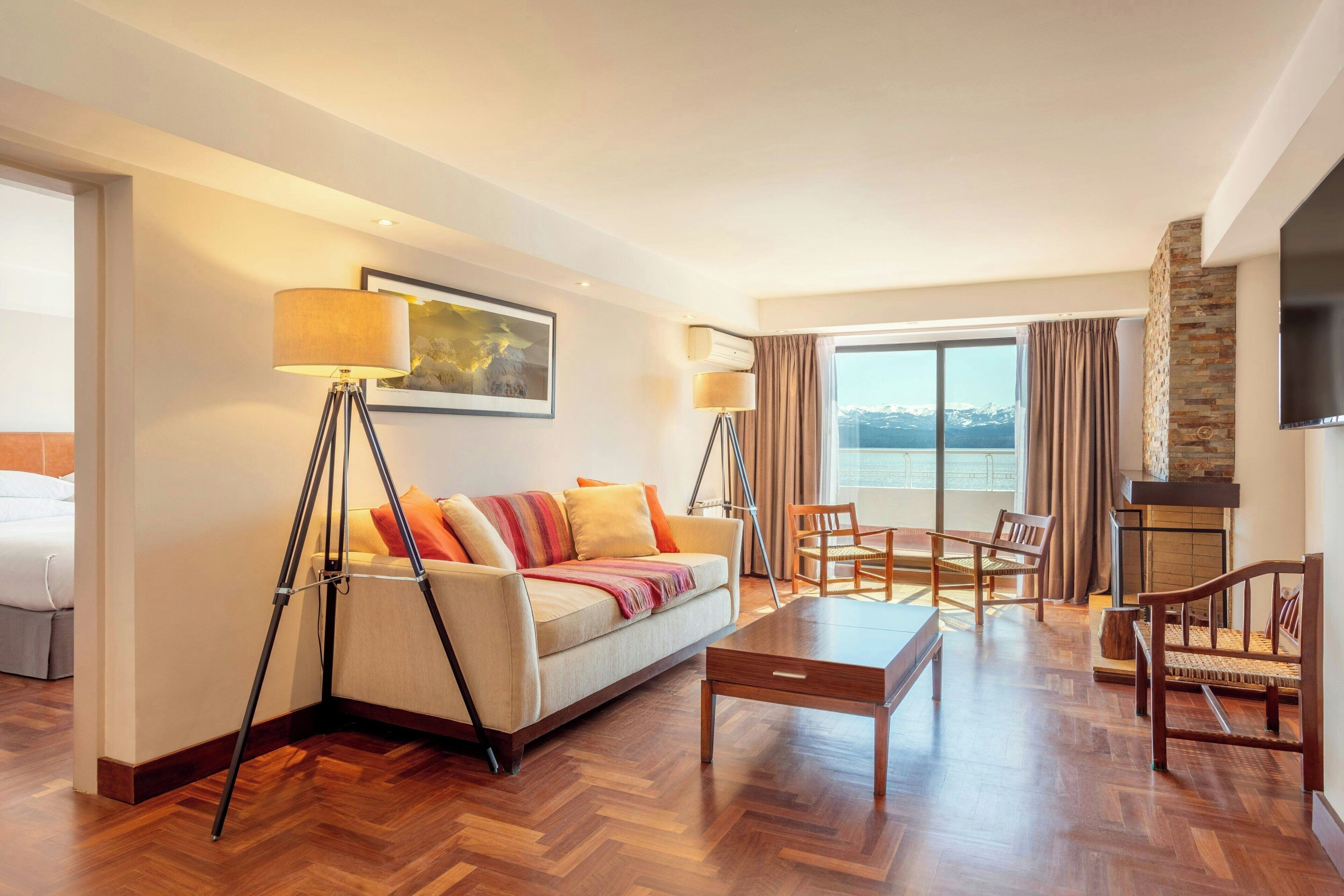Habitación de hotel con sofá, sillas, una mesa de centro, chimenea y un ventanal con vistas.