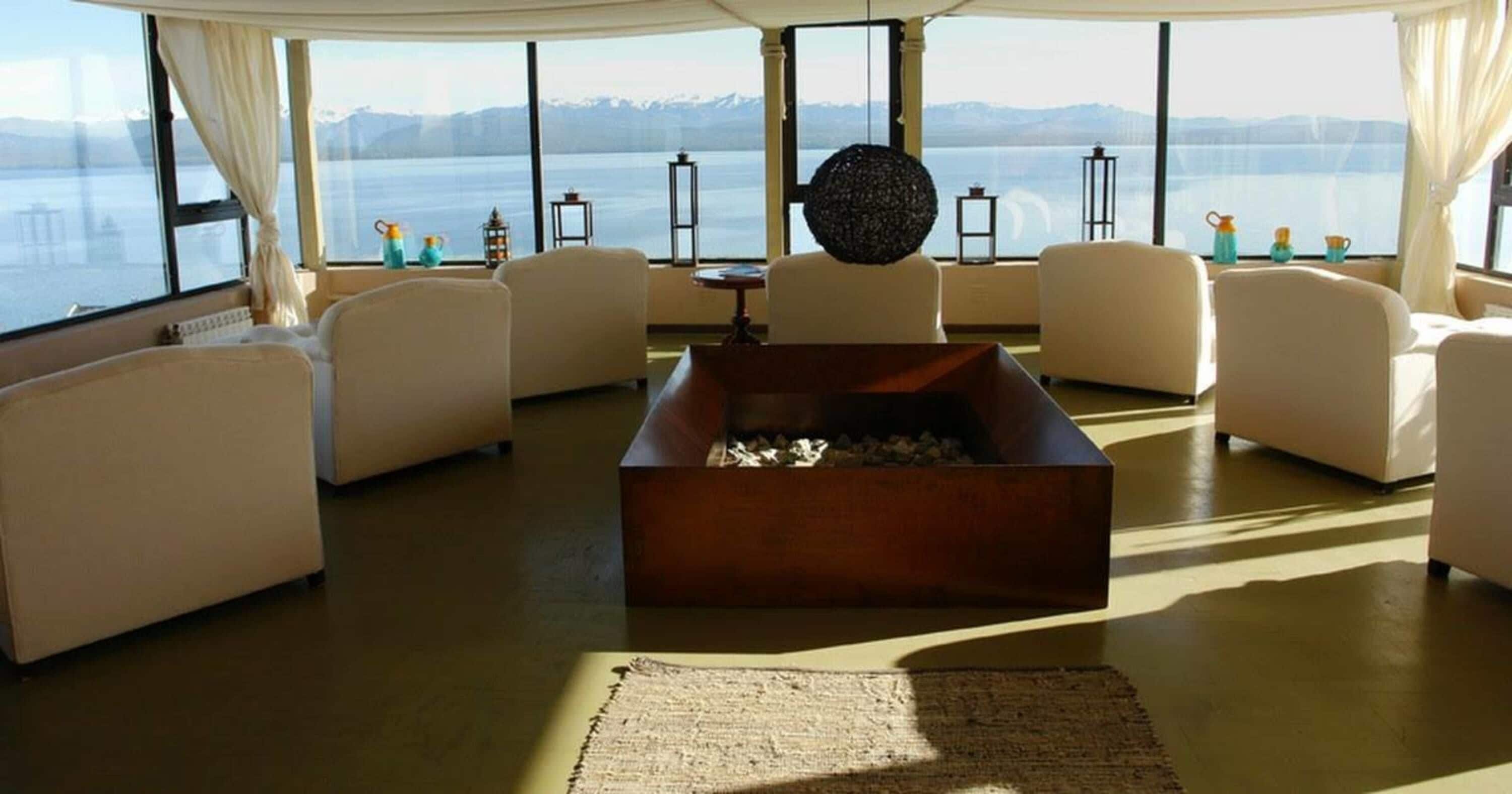 A spacious living room with a fireplace, comfortable seating, and large windows offering a view of a lake and mountains.