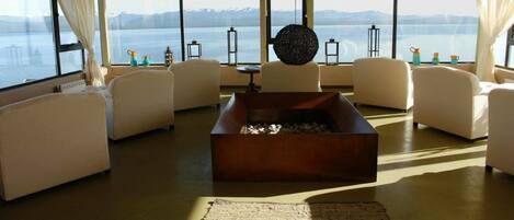 A spacious living room with a fireplace, comfortable seating, and large windows offering a view of a lake and mountains.