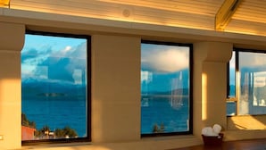 A pool area with large windows offering views of a body of water and distant mountains.