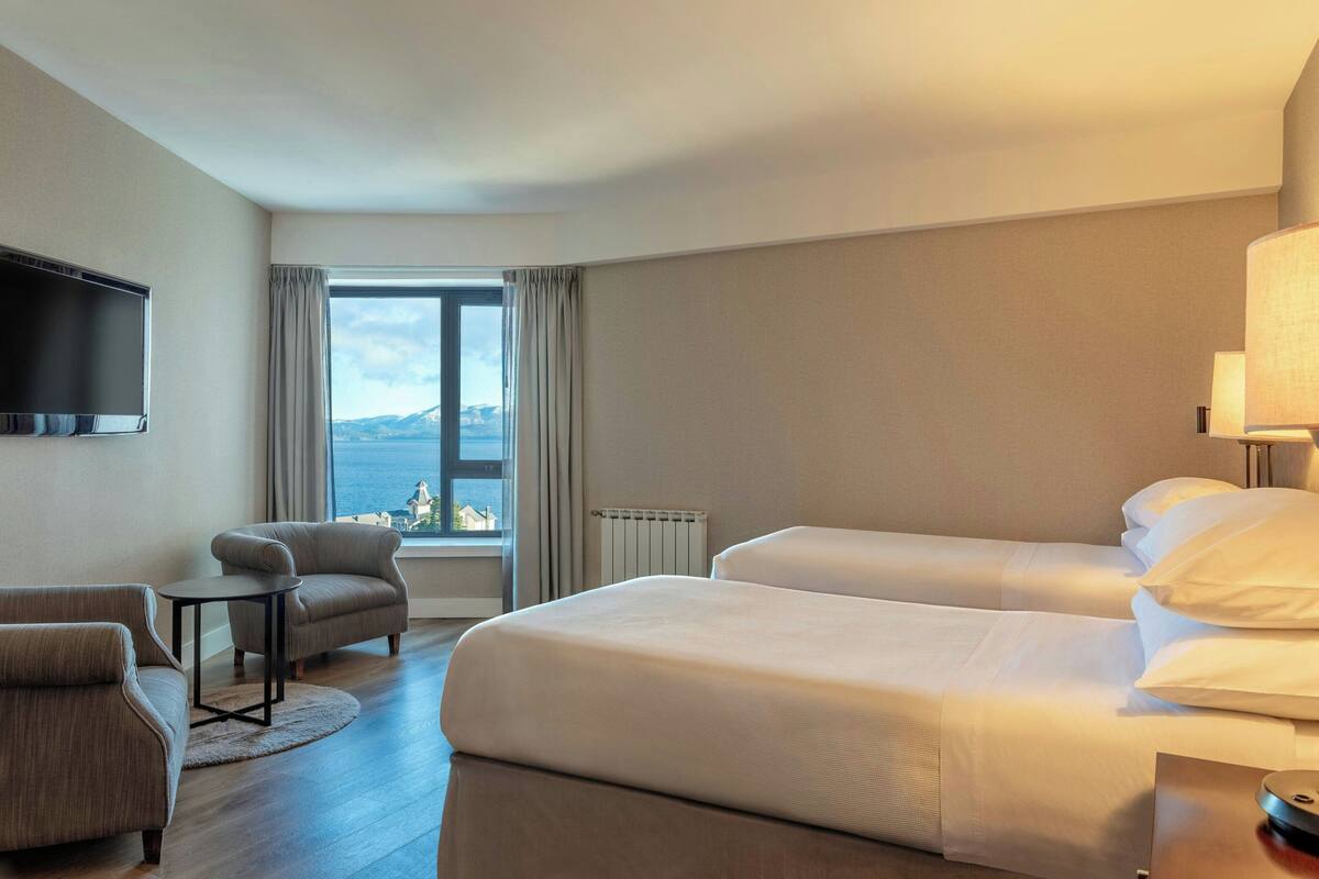 Une chambre d’hôtel avec deux lits, une télévision, une petite table et une vue sur la mer.