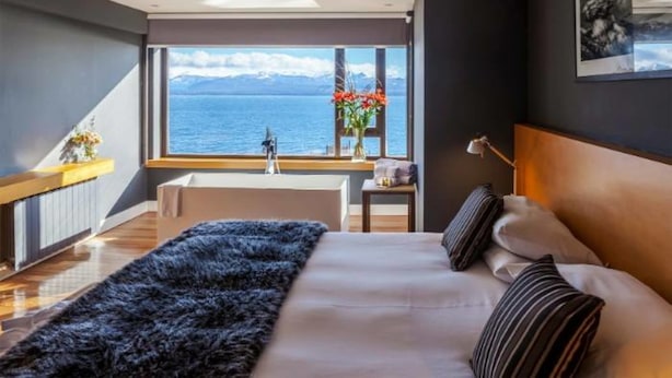 A modern bedroom with a large window offering a view of the sea and mountains.