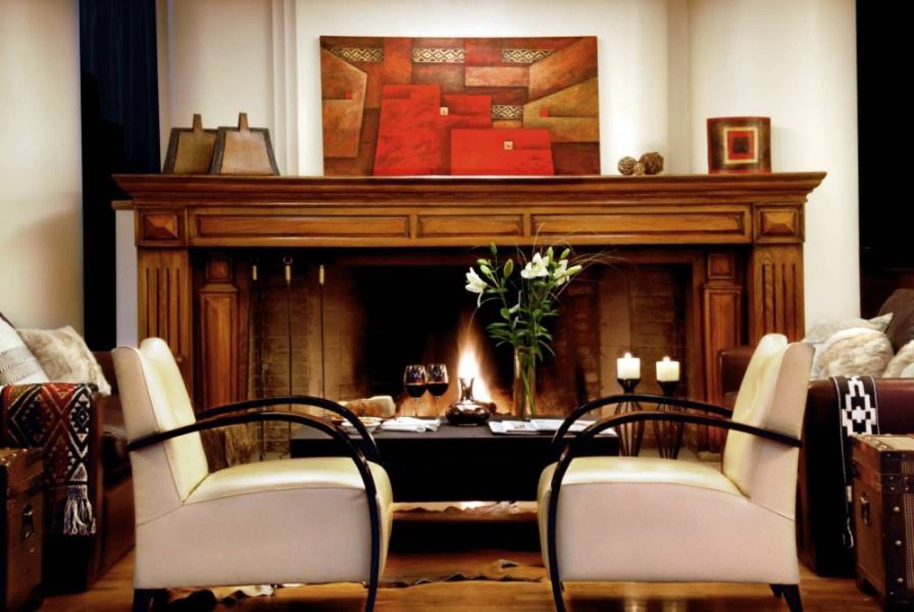 A cozy living room with a fireplace, two armchairs, a table with a vase of flowers, and a painting above the mantel.