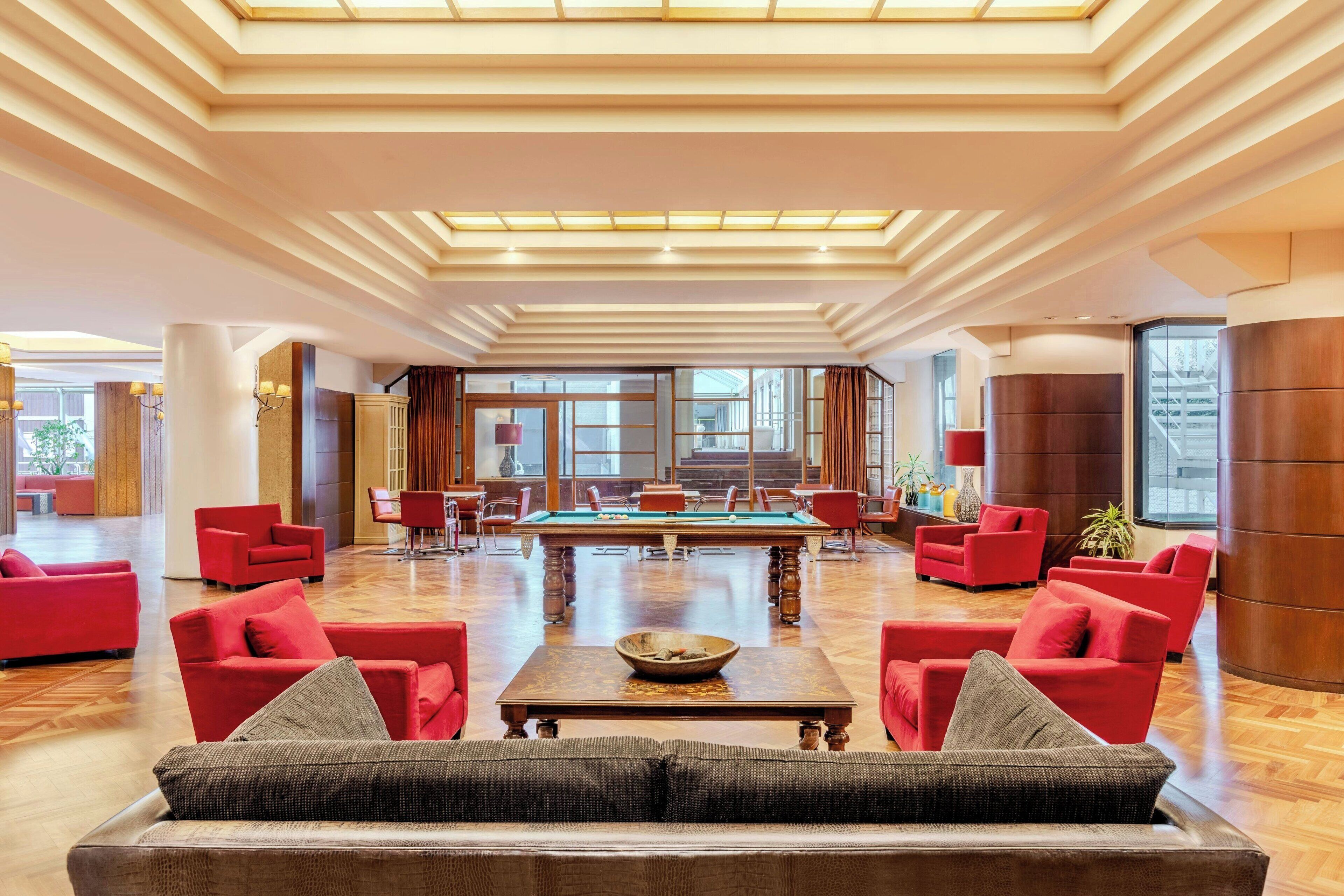 A spacious lobby with a pool table, red sofas, and a large window providing natural light.