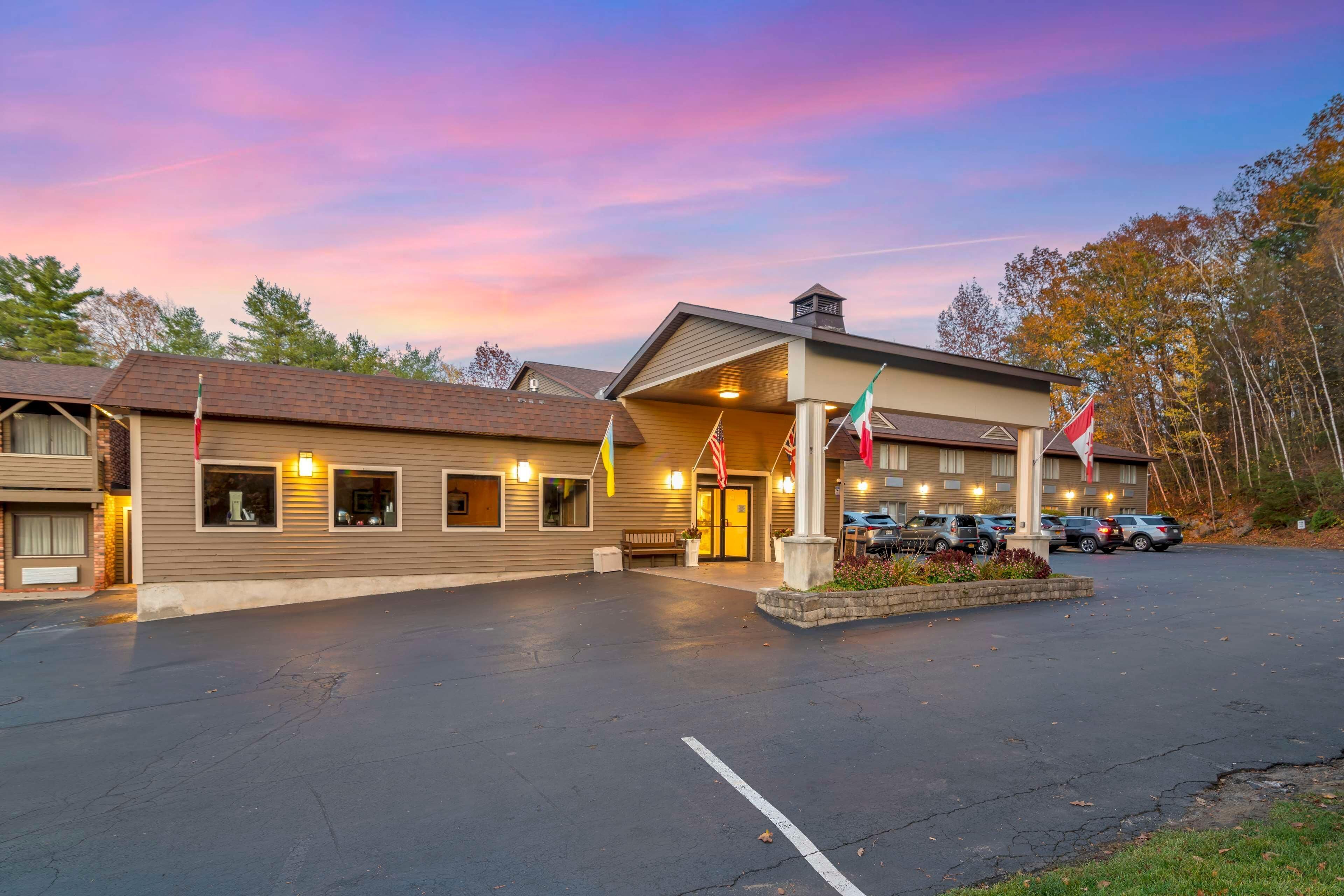 A hotel with a parking lot, multiple flags, and a sunset sky.