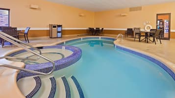 En hotels swimmingpool med fliset kant, et loungeområde med borde og stole, samt en automater.