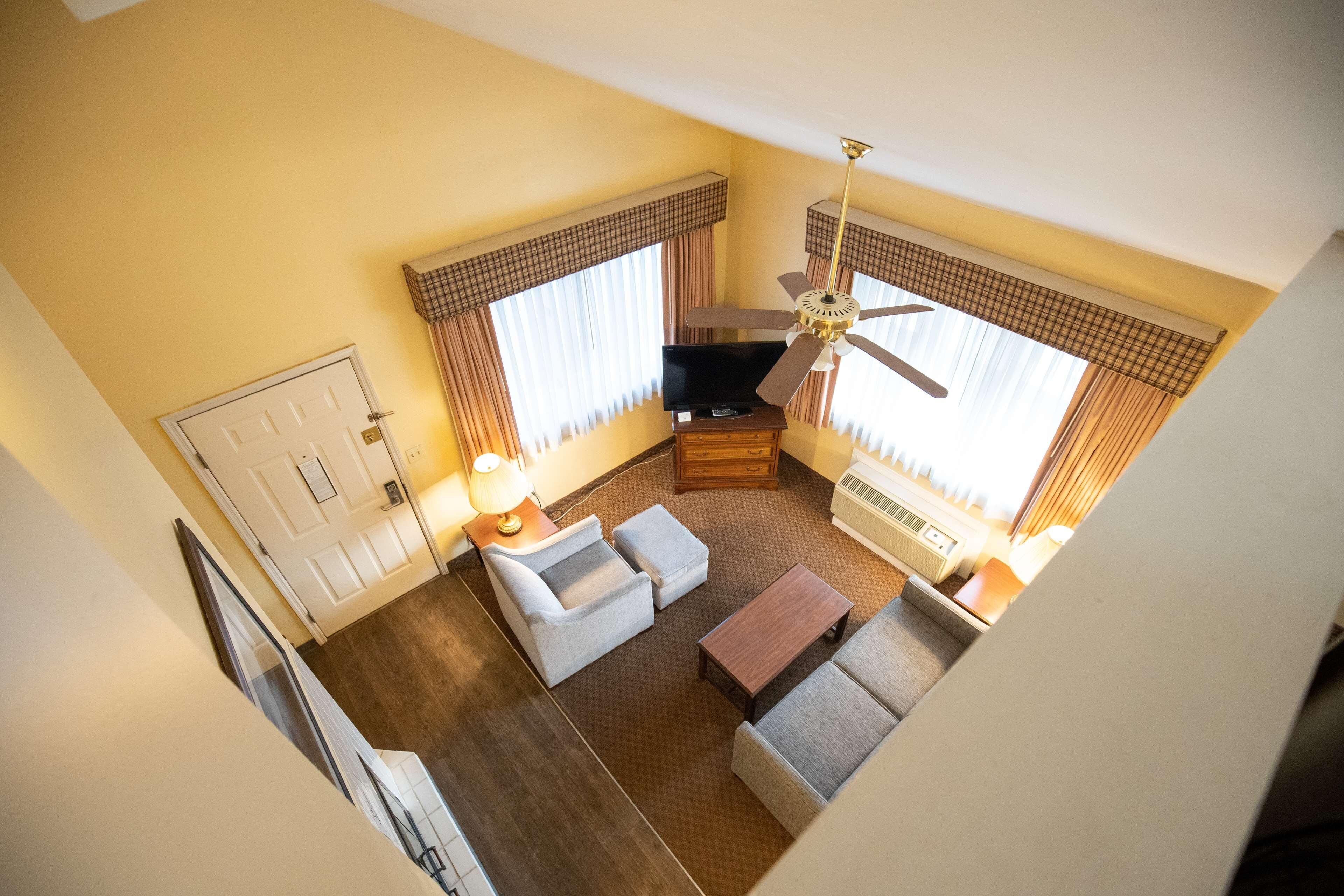 Habitación de hotel con sofá, sillón y una mesita. Cuenta con un ventilador de techo, un televisor y una ventana con cortinas.