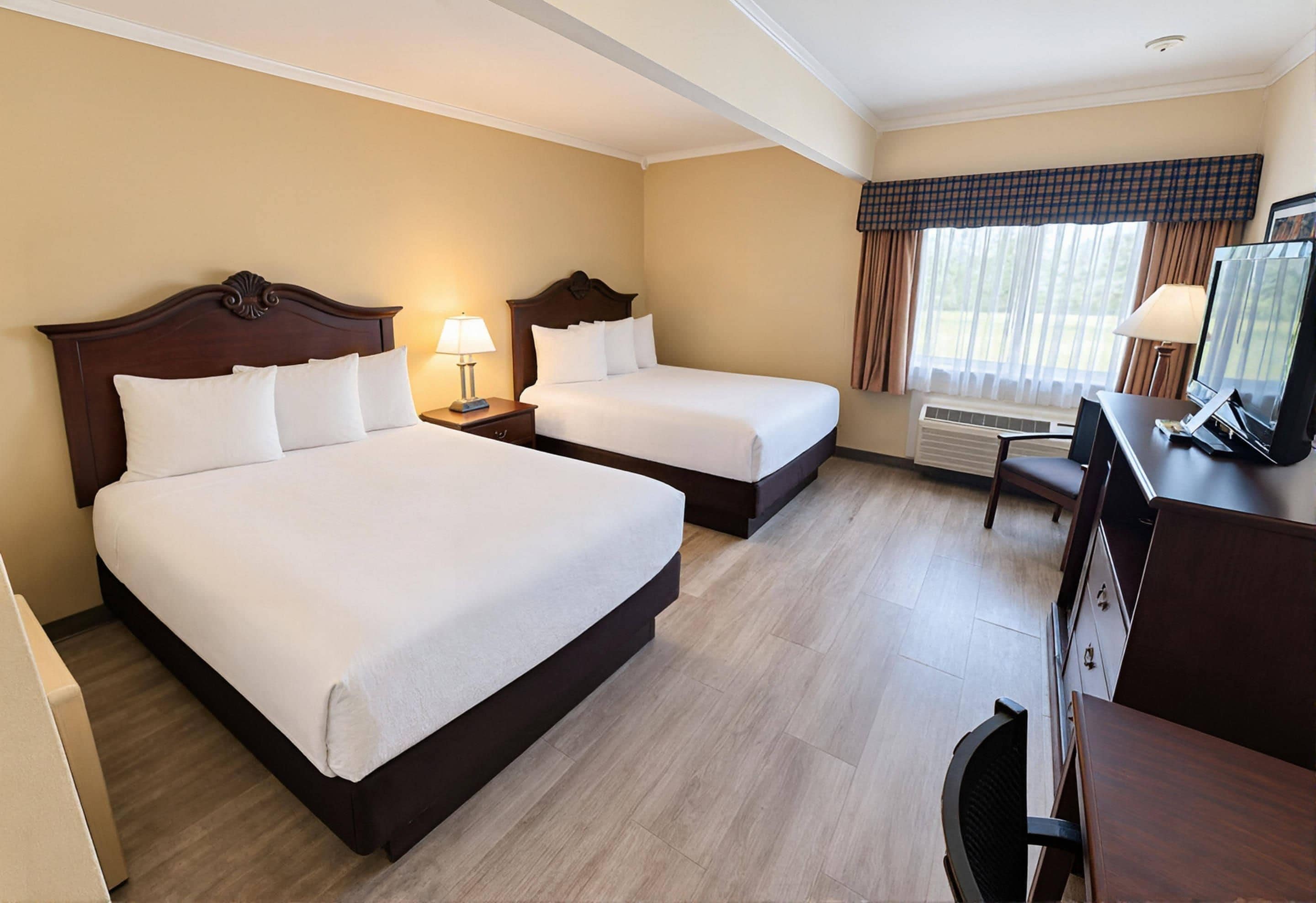 Een hotelkamer met twee bedden, een bureau met een televisie en een raam met gordijnen.