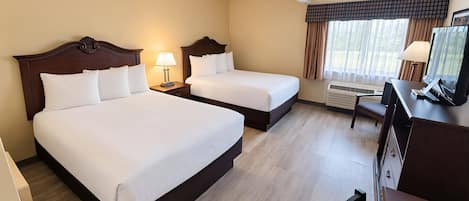 A hotel room with two beds, a desk with a television, and a window with curtains.