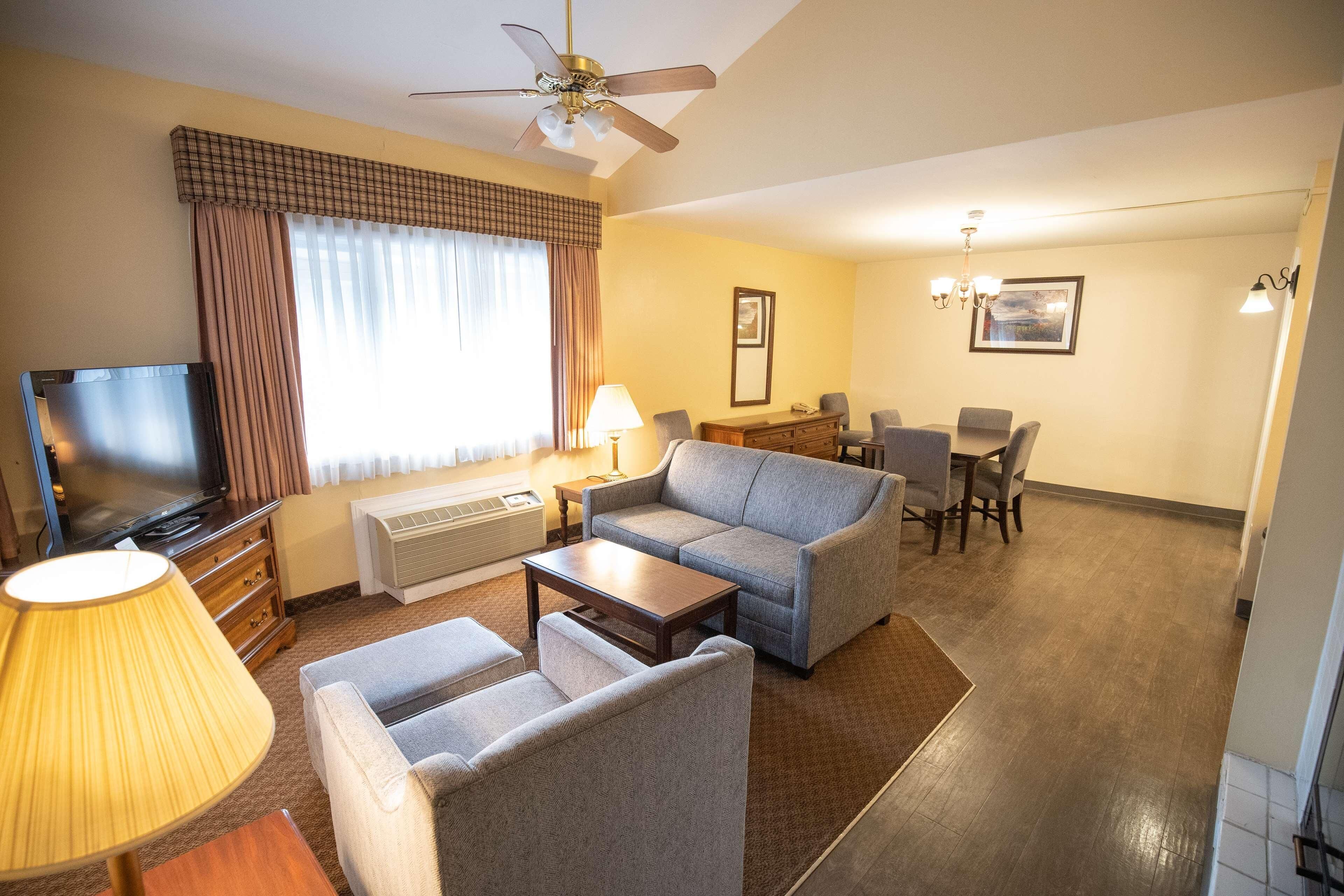 Een hotelkamer met televisie, bank, fauteuil, eettafel en stoelen.