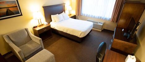A hotel room with a bed, a chair, a desk, a lamp, a clock, and a window with curtains.