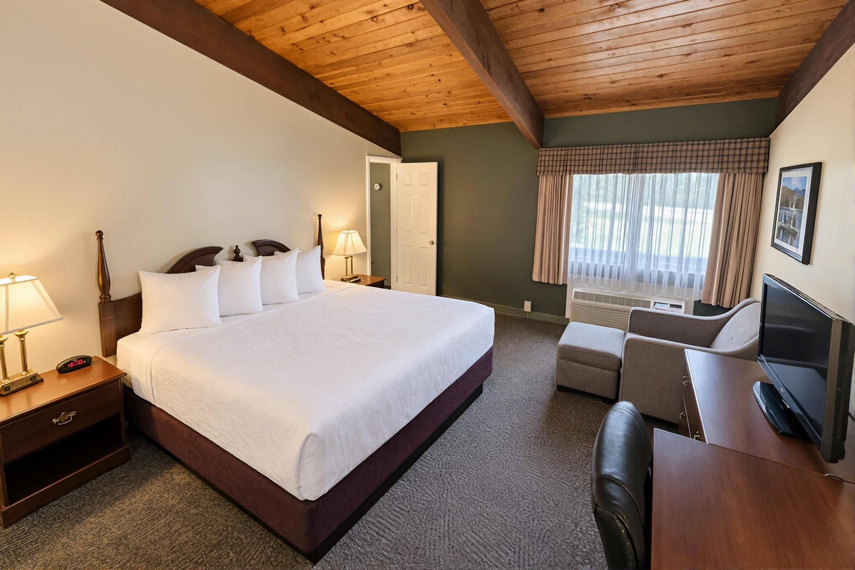 Habitación de hotel con una cama grande, lámparas de noche, un escritorio con televisor y una ventana con cortinas.