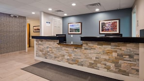 A reception desk with a stone wall, two framed pictures, and a door in the background.