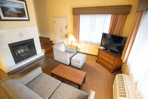 A hotel room with a fireplace, a television, a sofa, a coffee table, and a window with curtains. - Skyline Hotel Lake George (Lake George)