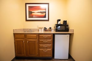 A compact kitchen with wooden cabinets, a white refrigerator, a microwave, and a coffee maker on the countertop.