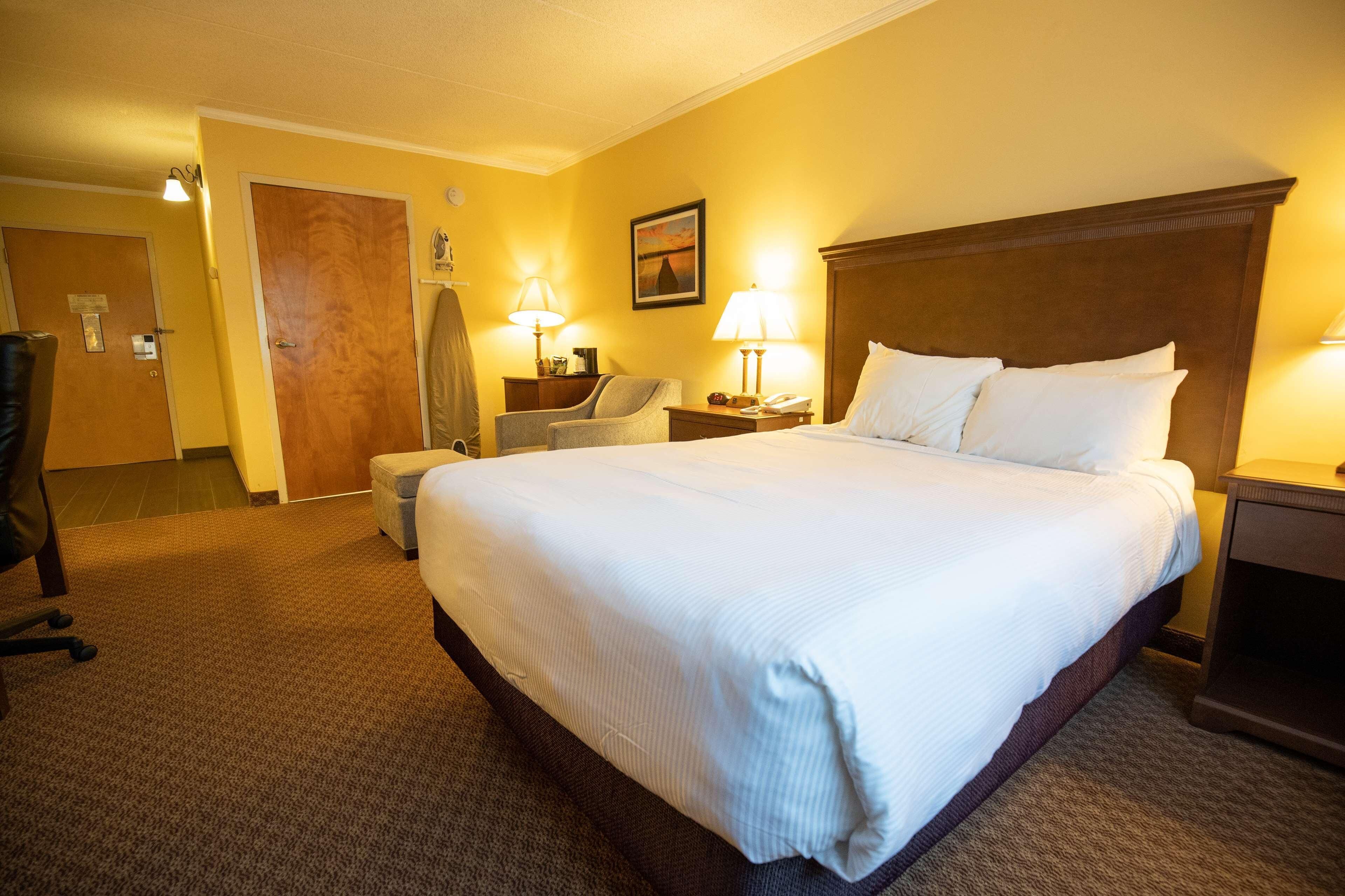 A hotel room with a large bed, a desk, a chair, a lamp, and a door.