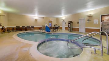 En indendørs swimmingpool med et boblebad, siddepladser og en dør til omklædningsrum.