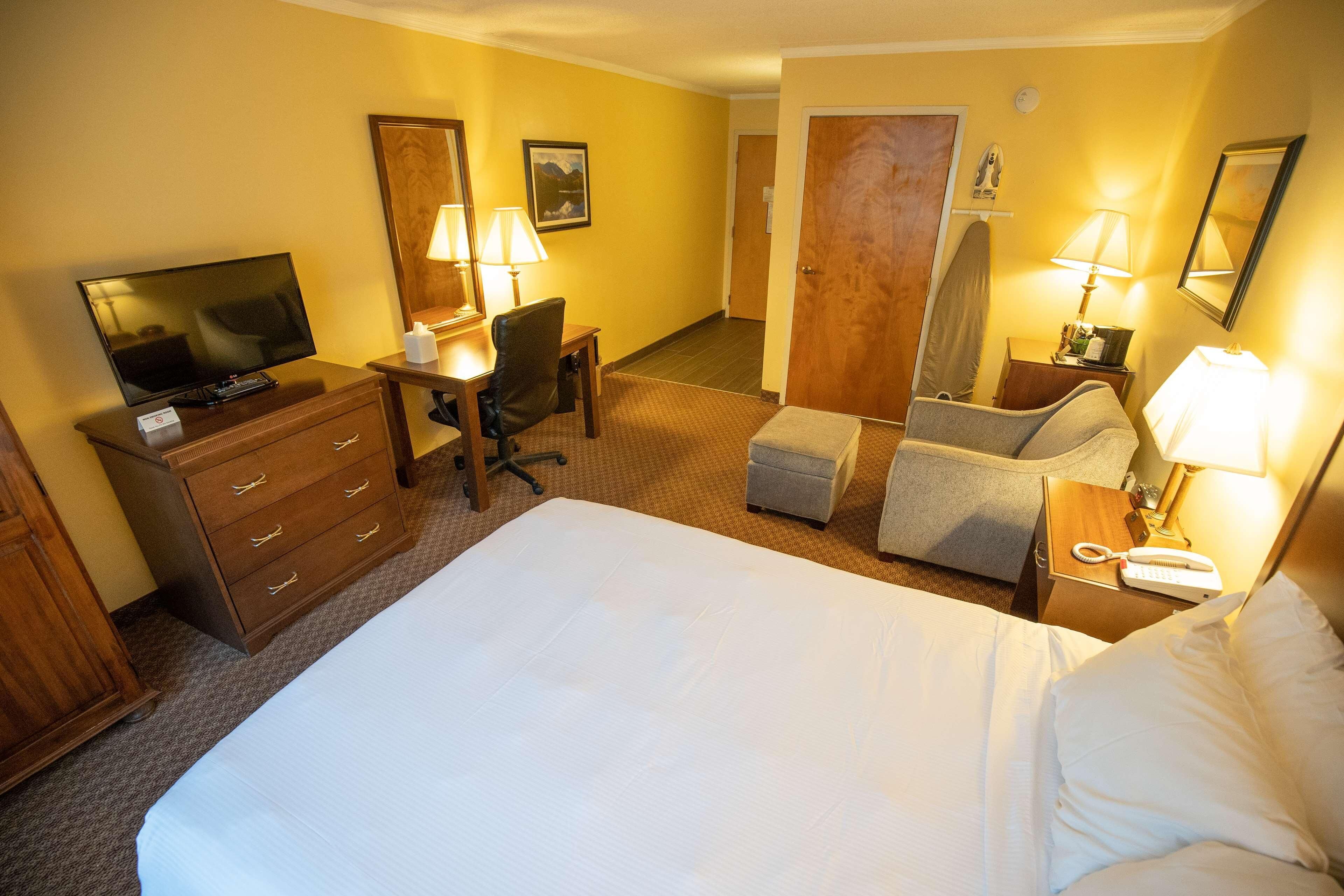 A hotel room with a large bed, a desk with a chair, a television, and two lamps.