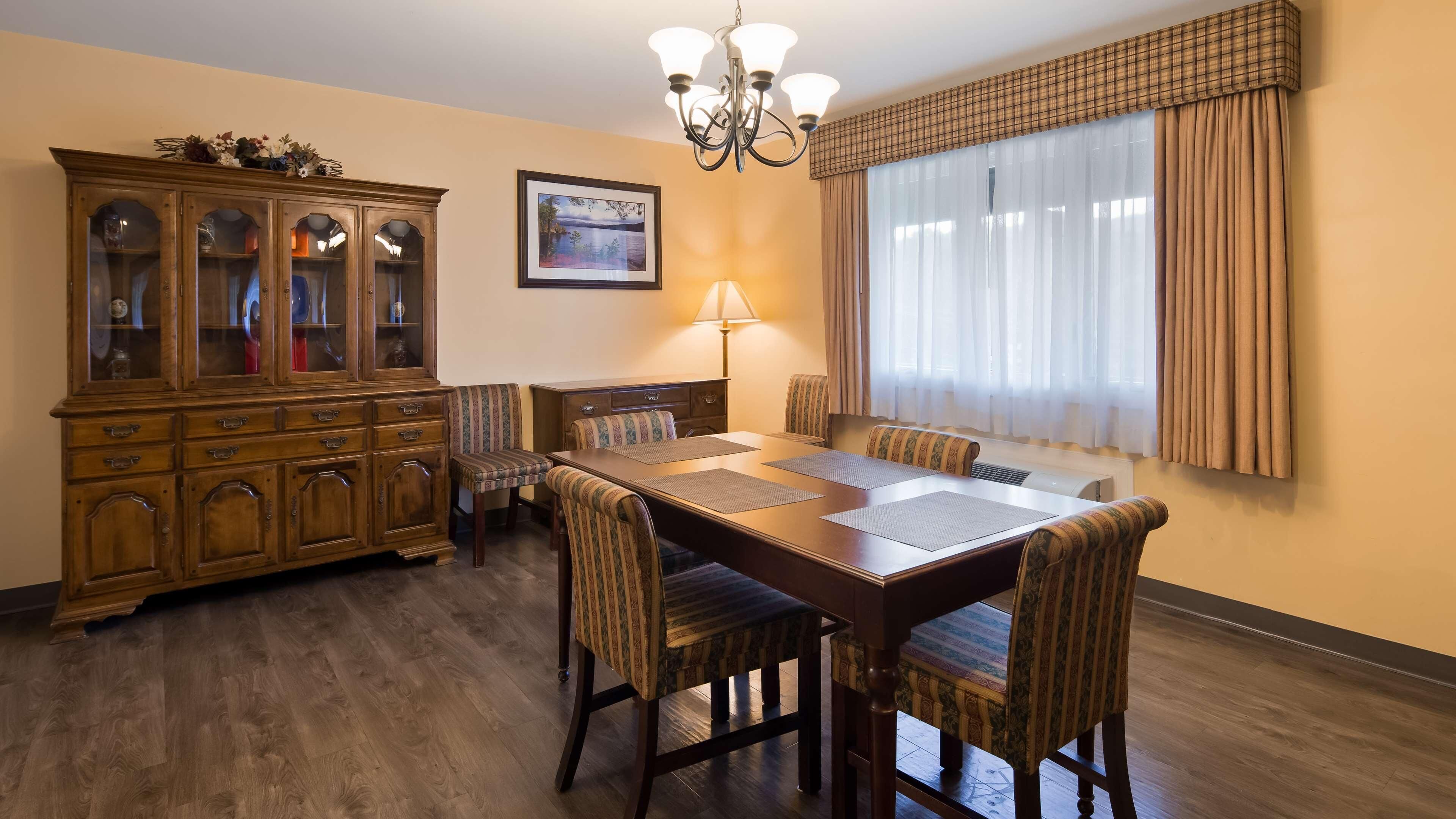 A dining room with a wooden table, chairs, a cabinet, a chandelier, and a window with curtains.