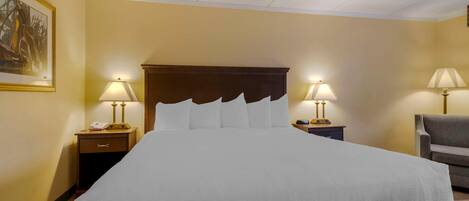 A hotel room with a large bed, two bedside tables with lamps, a chair, and a painting on the wall.