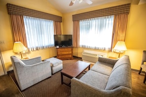 A hotel room with a flat-screen TV, two armchairs, a sofa, a wooden coffee table, and a heater.