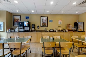 A breakfast area with tables, chairs, a juice bar, and a refrigerator with food items. - Skyline Hotel Lake George (Lake George)