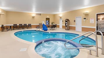 An indoor swimming pool with a hot tub, seating area, and a door with an emergency exit sign.