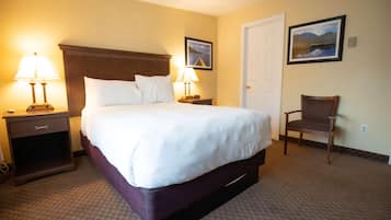 A hotel room with a large bed, two bedside tables with lamps, a chair, and a door.