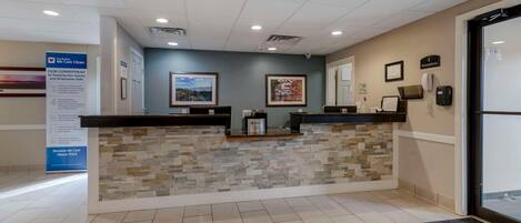 A reception desk with a stone facade, a framed landscape painting above it, and a sign on the wall to the left.