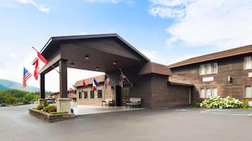 A building with a covered entrance, multiple flags, outdoor seating, and a parking area.