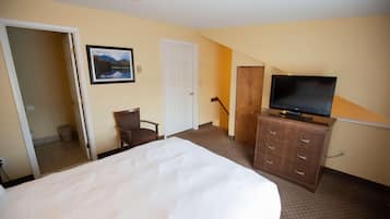 A hotel room with a large bed, a television on a dresser, a chair, and a door leading to another room.