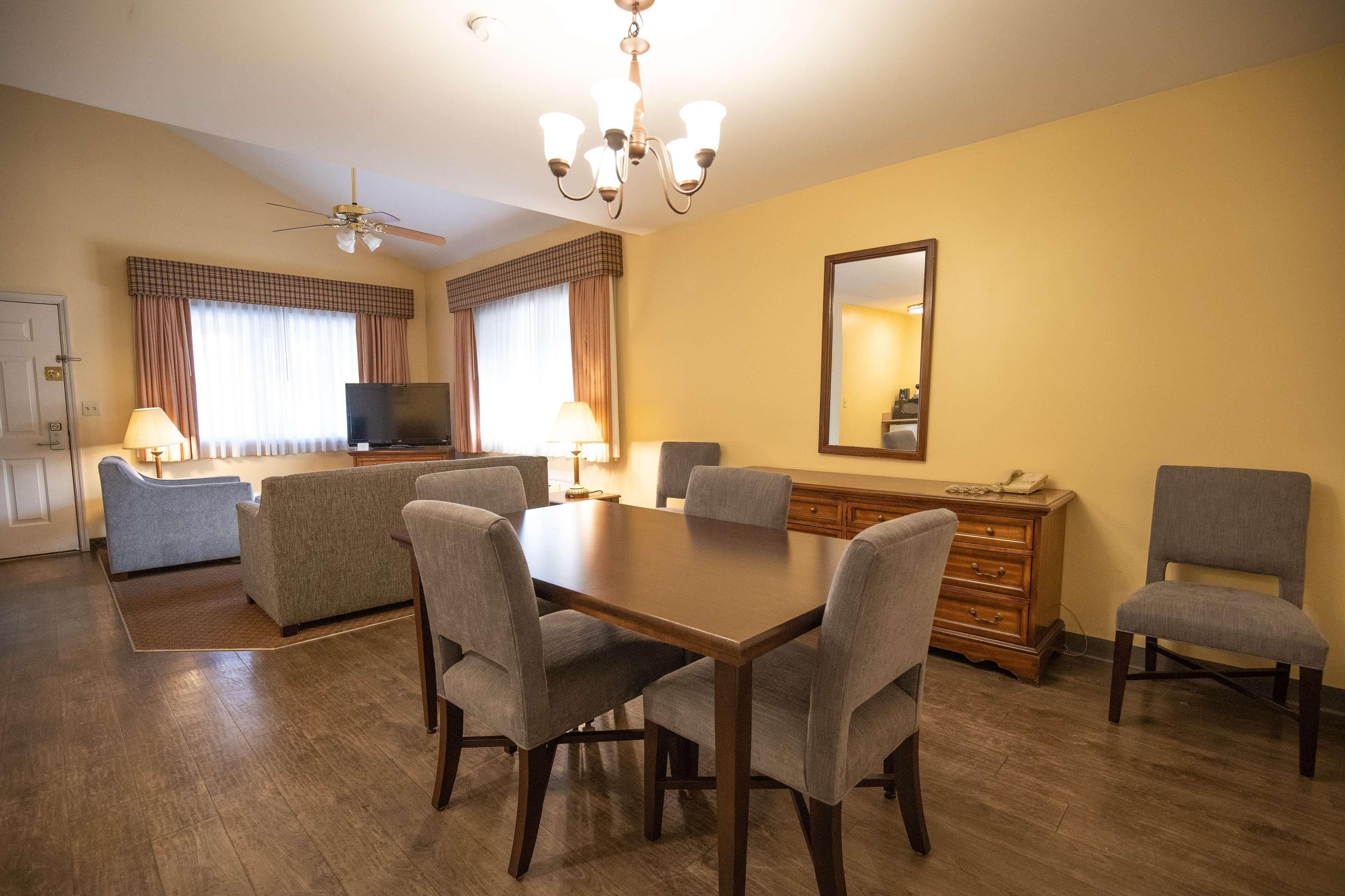Une chambre d’hôtel équipée d’une table à manger, de chaises, d’un téléviseur, d’un ventilateur de plafond et d’un grand miroir.