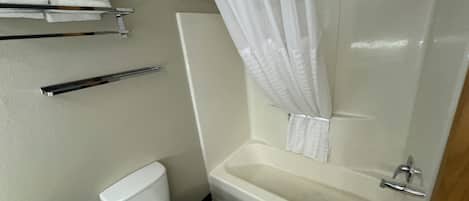 A bathroom with a white toilet, a bathtub with a shower curtain, and a towel rack with towels.