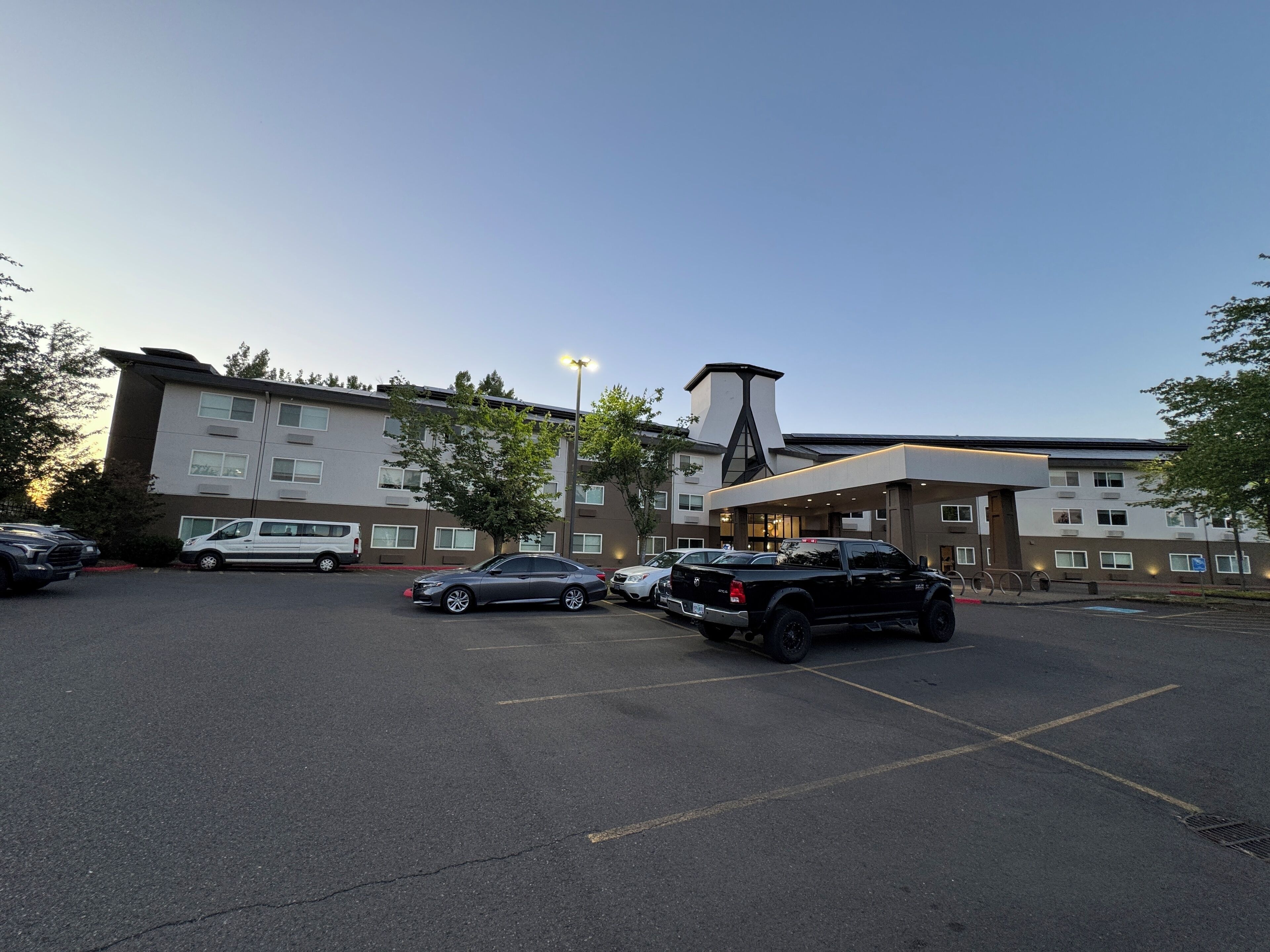 A parking lot with several cars and a building with multiple floors and a distinctive architectural feature.